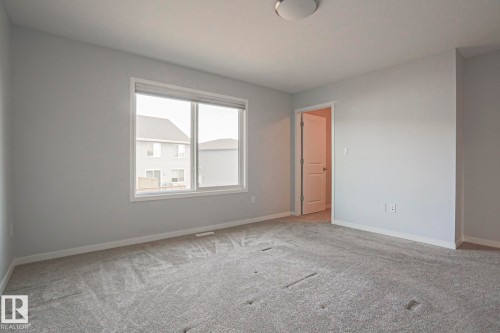 Spacious room featuring light gray carpeting, neutral wall paint, a large window with white trim, and a contemporary flush-mount ceiling light - 4314 Cooke Lane, Edmonton, AB - Indoor Photo Showing Other Room