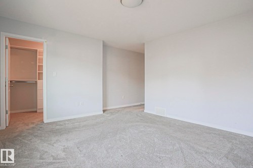 Neutral-toned room featuring light gray carpeting, white baseboards, and a built-in closet system with shelving and hanging rods - 4314 Cooke Lane, Edmonton, AB - Indoor Photo Showing Other Room