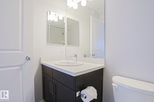 Contemporary bathroom vanity featuring a white countertop, undermount sink, and dark wood-finish cabinetry with brushed nickel hardware - 4314 Cooke Lane, Edmonton, AB - Indoor Photo Showing Bathroom