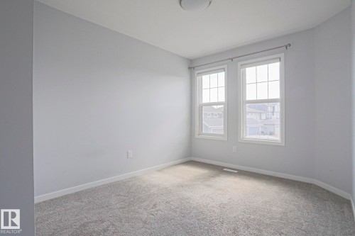 Light gray walls with white trim, two sash windows, gray carpet flooring, and a flush mount ceiling light - 4314 Cooke Lane, Edmonton, AB - Indoor Photo Showing Other Room
