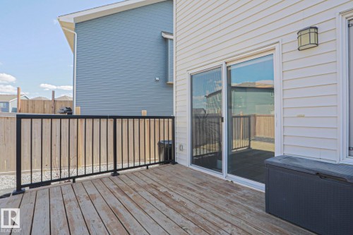 Outdoor wood-finish deck featuring a black metal railing, sliding glass patio door, and exterior wall light - 4314 Cooke Lane, Edmonton, AB - Outdoor With Deck Patio Veranda With Exterior