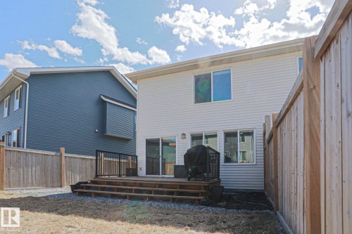 Rear exterior featuring white horizontal siding, a multi-level wood deck with black metal railings, and a sliding glass door - 4314 Cooke Lane, Edmonton, AB - Outdoor With Exterior
