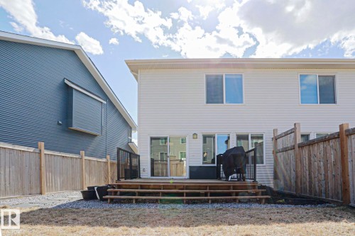 Rear exterior featuring a wood deck with black metal railings, white vinyl siding, multiple windows, and a sliding glass door - 4314 Cooke Lane, Edmonton, AB - Outdoor With Exterior