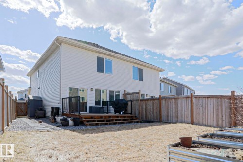 Rear exterior with white siding, showcasing a wooden deck with black metal railings, a gravel pathway, and a fully fenced perimeter - 4314 Cooke Lane, Edmonton, AB - Outdoor