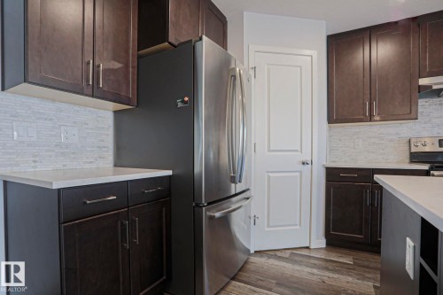 Kitchen featuring dark wood cabinetry, light countertops, a mosaic tile backsplash, stainless steel refrigerator, and wood-finish flooring - 4314 Cooke Lane, Edmonton, AB - Indoor Photo Showing Kitchen