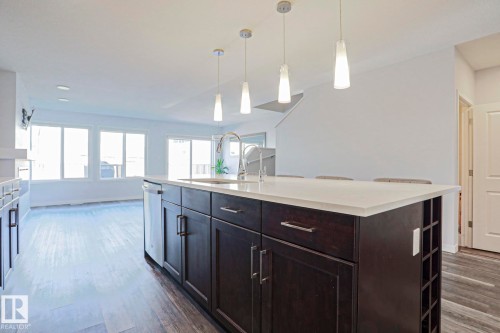 Kitchen island featuring dark wood cabinetry, a white countertop, and an integrated stainless steel sink with a gooseneck faucet - 4314 Cooke Lane, Edmonton, AB - Indoor Photo Showing Kitchen With Upgraded Kitchen