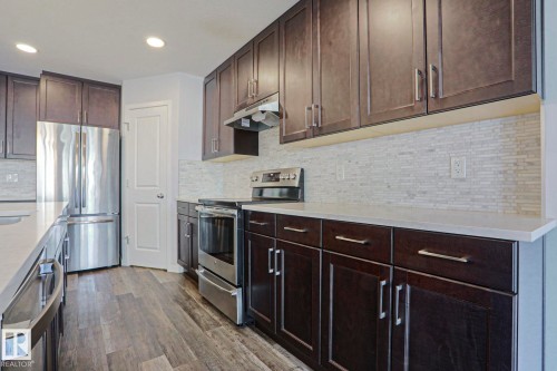 Kitchen featuring dark wood-finish cabinetry with brushed nickel hardware, light-toned countertops, and a full stainless steel appliance package - 4314 Cooke Lane, Edmonton, AB - Indoor Photo Showing Kitchen With Stainless Steel Kitchen With Upgraded Kitchen