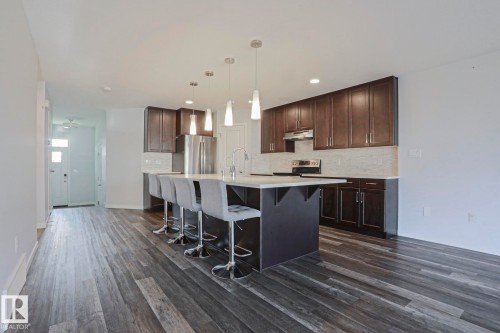 Open-concept kitchen featuring an island with pendant lighting, dark wood cabinetry, white subway tile backsplash, and stainless steel appliances - 4314 Cooke Lane, Edmonton, AB - Indoor Photo Showing Kitchen With Stainless Steel Kitchen With Upgraded Kitchen