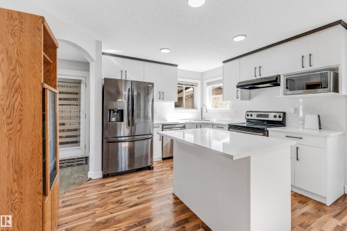 Contemporary kitchen featuring white cabinetry, a central island with a solid surface countertop, stainless steel appliances, and wood-finish flooring - 1921 119A Street, Edmonton, AB - Indoor Photo Showing Kitchen With Upgraded Kitchen