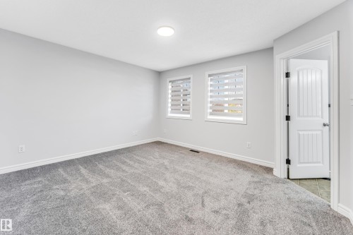 Light gray carpeted room with light gray walls, two windows featuring horizontal blinds, and a white six-panel interior door - 1921 119A Street, Edmonton, AB - Indoor Photo Showing Other Room