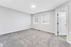 Light gray carpeted room with light gray walls, two windows featuring horizontal blinds, and a white six-panel interior door - 