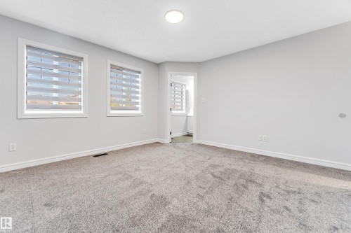 Spacious room featuring neutral carpeting, two windows with horizontal blinds, light gray wall paint, and white trim molding - 1921 119A Street, Edmonton, AB - Indoor Photo Showing Other Room
