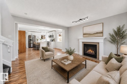 Open-concept living space featuring wood-finish flooring, a contemporary fireplace with a white mantel, and track lighting - 1921 119A Street, Edmonton, AB - Indoor Photo Showing Living Room With Fireplace
