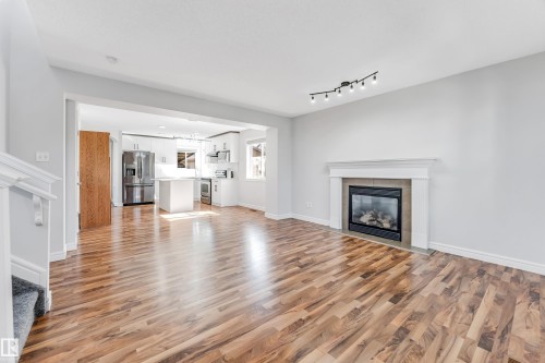Open-concept living area featuring wood-finish flooring, a contemporary fireplace with a white mantel, and track lighting - 1921 119A Street, Edmonton, AB - Indoor Photo Showing Living Room With Fireplace