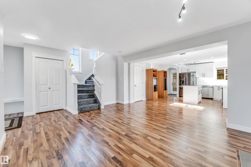 Open concept living area featuring wood-finish flooring, a carpeted staircase, and a kitchen with white cabinetry, stainless steel appliances, and a central island - 1921 119A Street, Edmonton, AB - Indoor