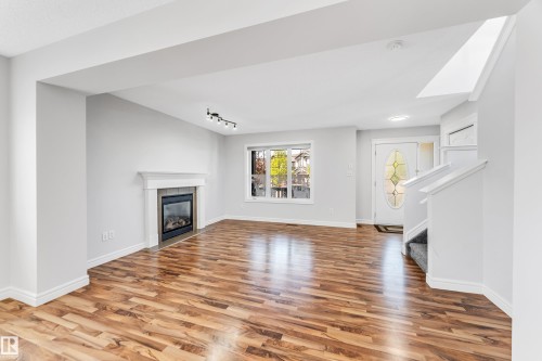 Spacious interior featuring wood-finish flooring, a contemporary fireplace with mantel, white trim throughout, a front entry door with decorative glass, and a carpeted stairway - 1921 119A Street, Edmonton, AB - Indoor Photo Showing Living Room With Fireplace