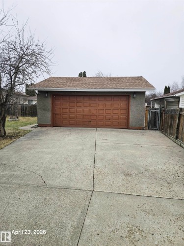 Detached garage with a brown panel door, grey stucco exterior, and asphalt shingle roof - 20 Hunt Road, Edmonton, AB - Outdoor