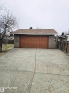 Detached garage with a brown panel door, grey stucco exterior, and asphalt shingle roof - 