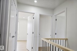Bright hallway featuring a light wood railing with metal balusters, recessed lighting, and white paneled doors with chrome hardware - 