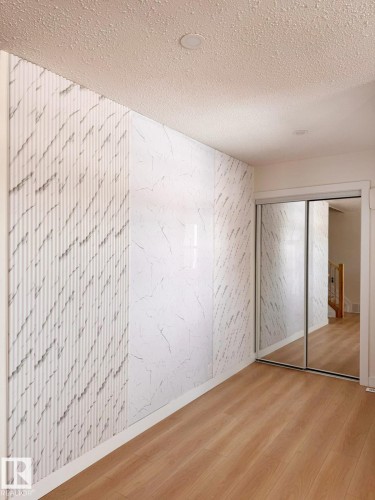 Textured accent wall with a geometric pattern, complemented by marble-effect panels, light wood-finish flooring, and mirrored closet doors - 20 Hunt Road, Edmonton, AB - Indoor Photo Showing Other Room