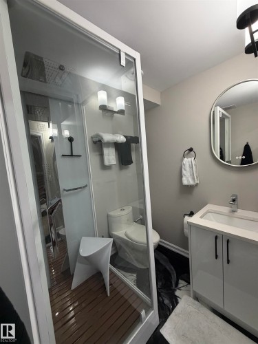 Contemporary bathroom featuring a glass-enclosed steam shower, epoxy flooring, a white vanity with integrated sink, and a lighted circular wall mirror. - 5204 4 Avenue, Edmonton, AB - Indoor Photo Showing Bathroom