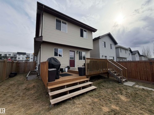 Rear exterior featuring light-toned horizontal siding, a multi-level wood deck with stairs, a dark red entry door, multiple windows, and a wood privacy fence - 5204 4 Avenue, Edmonton, AB - Outdoor With Deck Patio Veranda With Exterior