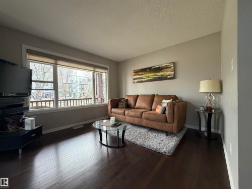 Spacious living area featuring large windows with roller blinds, dark wood-finish flooring, and light gray painted walls - 5204 4 Avenue, Edmonton, AB - Indoor Photo Showing Living Room