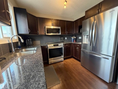 Kitchen featuring stainless steel appliances, dark wood-finish cabinetry, granite-style countertops, and wood-finish flooring - 5204 4 Avenue, Edmonton, AB - Indoor Photo Showing Kitchen With Stainless Steel Kitchen With Double Sink