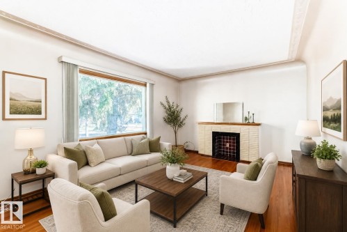 Spacious living area featuring a large picture window, wood-finish flooring, a white brick fireplace with a decorative tile insert, and crown molding - 11424 105 Street, Edmonton, AB - Indoor Photo Showing Living Room With Fireplace