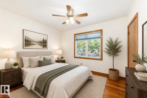 Bright bedroom featuring wood-finish flooring, a ceiling fan with integrated lighting, a window with natural wood trim, and a solid wood door - 11424 105 Street, Edmonton, AB - Indoor Photo Showing Bedroom