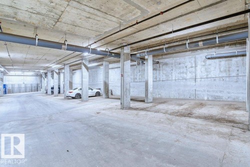 Spacious concrete parking garage featuring numerous structural columns, overhead utility pipes, and integrated lighting - 318 1316 Windermere Way, Edmonton, AB - Indoor Photo Showing Garage