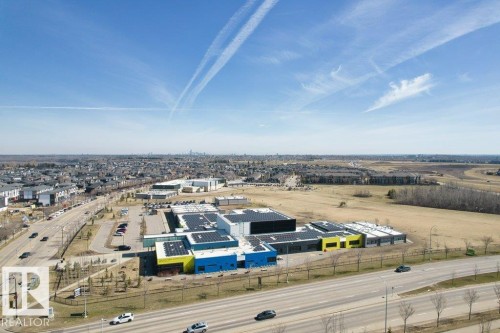 Modern commercial complex featuring a vibrant multi-color facade, extensive rooftop solar panel installations, and ample surface parking - 318 1316 Windermere Way, Edmonton, AB - Outdoor With View