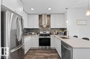 Modern kitchen featuring white shaker cabinetry, stainless steel appliances, wood-finish flooring, a mosaic tile backsplash, and light-toned countertops - 318 1316 Windermere Way, Edmonton, AB  - Indoor Photo Showing Kitchen With Stainless Steel Kitchen With Upgraded Kitchen 
