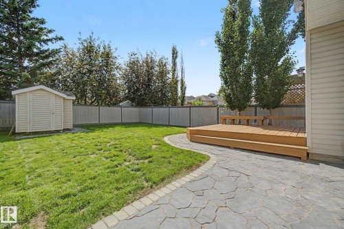 Expansive backyard featuring a wood deck with integrated seating, a flagstone patio, a manicured lawn, a detached storage shed, and a privacy fence - 8311 11 Avenue, Edmonton, AB 