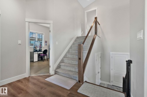 Carpeted staircase featuring a wood and glass railing, wood-finish flooring, and white trim throughout - 67 Enchanted Way Nw, St. Albert, AB - Indoor Photo Showing Other Room