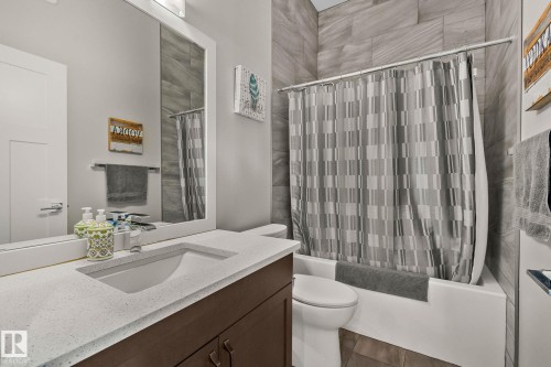 Bathroom featuring a white framed mirror, a vanity with a white speckled countertop, a rectangular undermount sink, a dark wood-finish cabinet, and a white bathtub with a gray tiled surround - 67 Enchanted Way Nw, St. Albert, AB - Indoor Photo Showing Bathroom