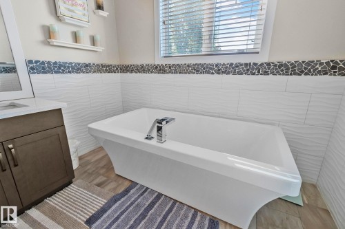 Freestanding soaking tub with chrome fixtures, set against textured white subway tile and a decorative mosaic border - 67 Enchanted Way Nw, St. Albert, AB - Indoor Photo Showing Bathroom