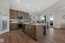 Spacious kitchen featuring wood-finish flooring, an expansive island with a sink, quartz countertops, stainless steel appliances, and a mosaic tile backsplash - 67 Enchanted Way Nw, St. Albert, AB  - Indoor Photo Showing Kitchen 