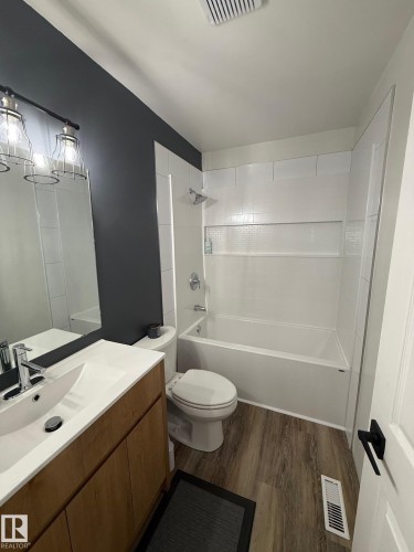 Bathroom featuring a wood-finish vanity with an integrated white sink, chrome faucet, and a large wall mirror - 5108 58 Avenue, Elk Point, AB - Indoor Photo Showing Bathroom