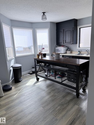 Kitchen area featuring wood-finish flooring, a contemporary island with storage, black cabinetry, a stainless steel sink, and multiple windows - 5108 58 Avenue, Elk Point, AB - Indoor Photo Showing Office