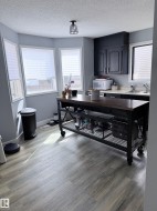 Kitchen area featuring wood-finish flooring, a contemporary island with storage, black cabinetry, a stainless steel sink, and multiple windows - 