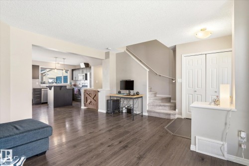Open-concept living space featuring wood-finish flooring, a contemporary kitchen with a center island, a carpeted staircase with a handrail, and built-in closet doors - 7114 22 Avenue, Edmonton, AB - Indoor Photo Showing Living Room