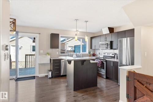 Kitchen featuring dark wood-finish cabinetry, stainless steel appliances, a center island with pendant lighting, light-toned countertops, and wood-finish flooring - 7114 22 Avenue, Edmonton, AB - Indoor Photo Showing Kitchen