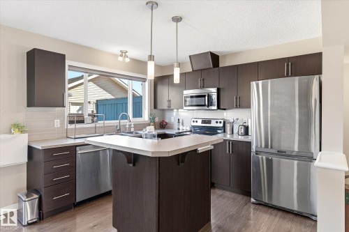 Modern kitchen featuring dark wood-finish cabinetry, stainless steel appliances, light-toned countertops, and wood-finish flooring - 7114 22 Avenue, Edmonton, AB - Indoor Photo Showing Kitchen With Upgraded Kitchen