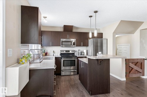 Kitchen featuring dark wood-finish cabinetry, stainless steel appliances, light-toned countertops, and wood-finish flooring - 7114 22 Avenue, Edmonton, AB - Indoor Photo Showing Kitchen With Upgraded Kitchen