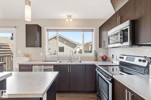 Contemporary kitchen featuring dark wood-finish cabinetry, stainless steel appliances, a double basin sink, light-toned countertops, and a white subway tile backsplash - 7114 22 Avenue, Edmonton, AB - Indoor Photo Showing Kitchen With Double Sink