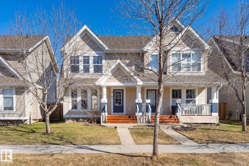 Duplex property featuring a light-colored siding exterior, gabled rooflines, and a front porch with white railings - 7114 22 Avenue, Edmonton, AB - Outdoor With Deck Patio Veranda With Facade