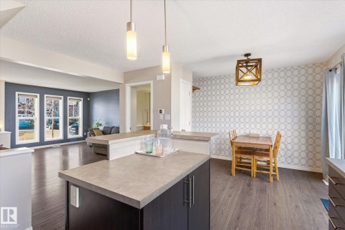 Open-concept kitchen and dining area featuring dark wood-finish flooring, two pendant lights over the island, and a geometric pattern accent wall - 7114 22 Avenue, Edmonton, AB - Indoor
