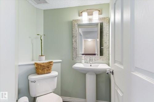Powder room featuring a pedestal sink with chrome faucet, a rectangular mirror with a textured frame, a two-bulb vanity light, and light green painted walls - 7114 22 Avenue, Edmonton, AB - Indoor Photo Showing Bathroom