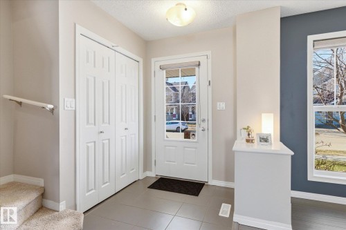 Foyer featuring large format tile flooring, a multi-pane front door, a built-in closet with bifold doors, a white handrail, and a window with a blue accent wall - 7114 22 Avenue, Edmonton, AB - Indoor Photo Showing Other Room